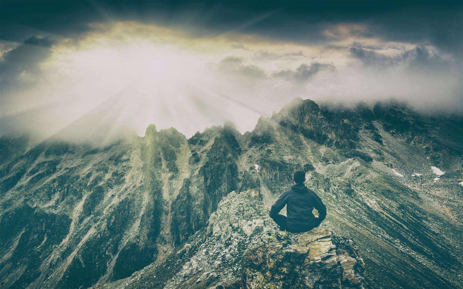Persona meditando en la cima de una montaña entre la niebla, con la luz del amanecer