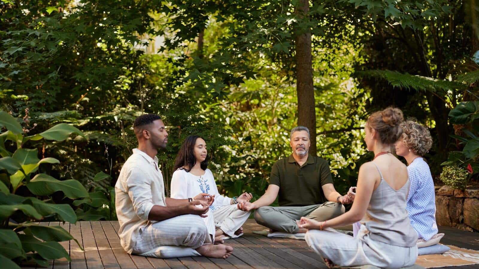 Grupo meditando sentado sobre una tarima de madera rodeada de bosque