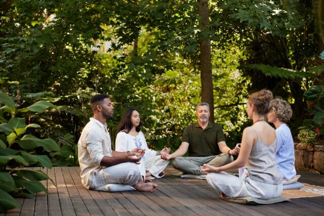 Grupo meditando sentado sobre una tarima de madera rodeada de bosque