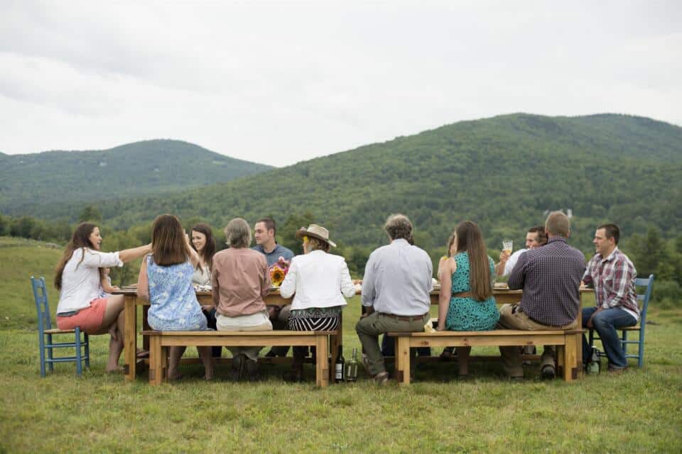Grupo comiendo en una mesa larga al aire libre con montañas al fondo