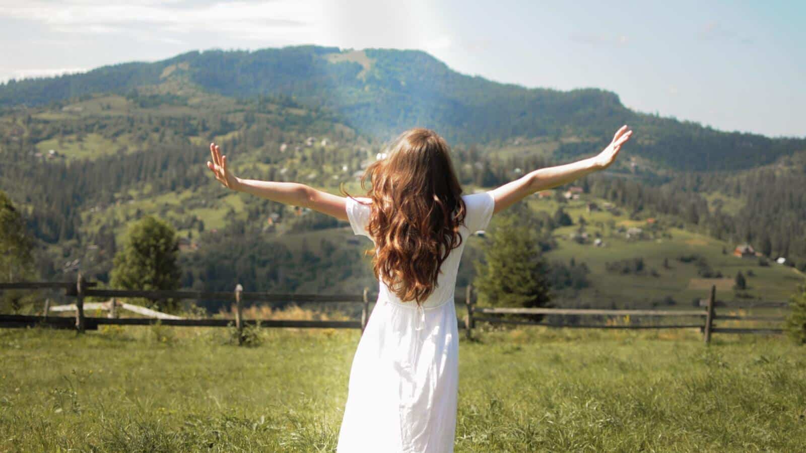 Mujer con los brazos abiertos frente a un paisaje de montaña