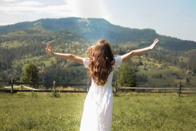 Mujer con los brazos abiertos frente a un paisaje de montaña