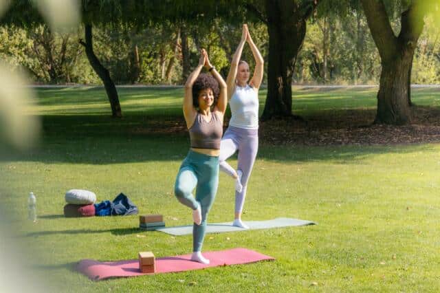 Dos personas practicando yoga en la postura del árbol en un parque
